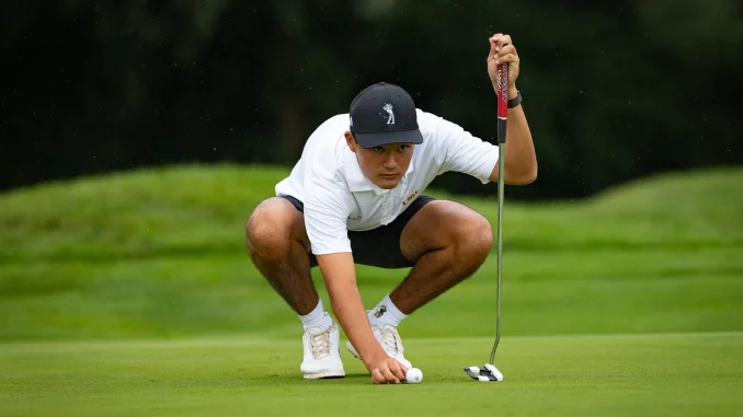 Golfer in a white polo and cap crouches on the green, lining up a putt with a putter near the ball.