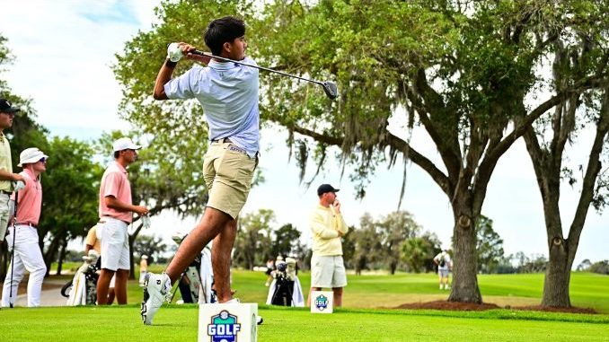 Golfer mid-swing on a tee with onlookers at a sunny golf course.