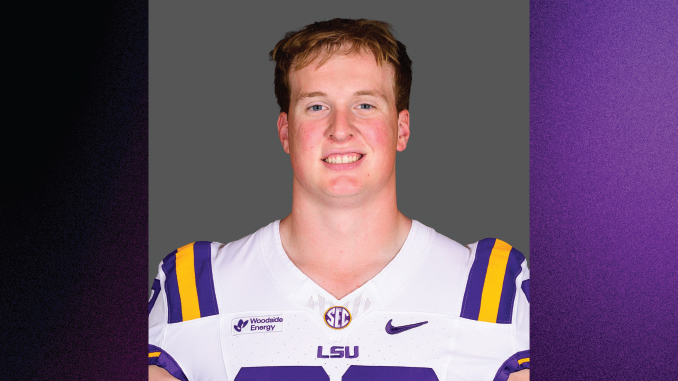 Portrait of a smiling male college football player in LSU white jersey with purple and gold stripes and shoulder pads, neutral gray background.