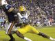 LSU defender in yellow pants tackles a ball carrier in a dark uniform near the sideline during a college football game.
