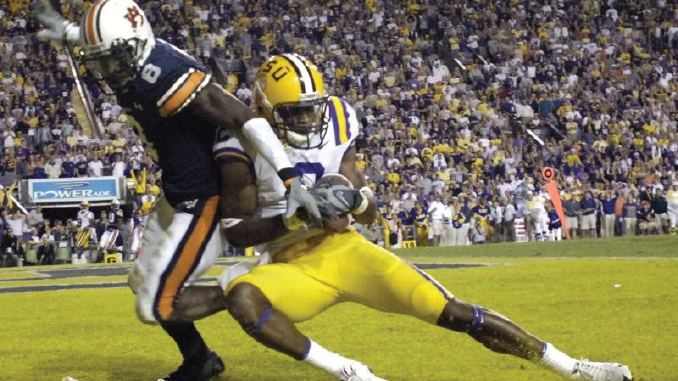 LSU defender in yellow pants tackles a ball carrier in a dark uniform near the sideline during a college football game.