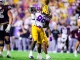 LSU football player in white jersey and gold pants collides with a Texas A&M defender during a college football game on a green field.