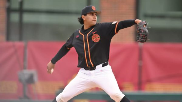 Right-handed pitcher in a black USC uniform with orange trim throws a pitch on the mound, glove up.