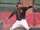 Right-handed pitcher in a black USC uniform with orange trim throws a pitch on the mound, glove up.