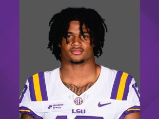 Portrait of a male LSU football player in a white jersey with purple and gold trim, against a gray background.