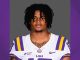 Portrait of a male LSU football player in a white jersey with purple and gold trim, against a gray background.