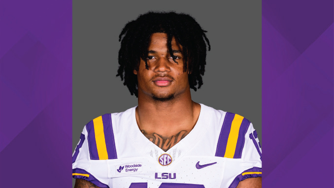 Portrait of a male LSU football player in a white jersey with purple and gold trim, against a gray background.