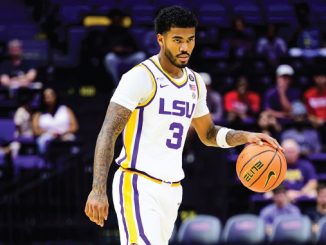LSU basketball player wearing #3 in a white uniform dribbles the ball on court with purple seats in the background behind him.” (shortened)