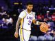 LSU basketball player wearing #3 in a white uniform dribbles the ball on court with purple seats in the background behind him.” (shortened)