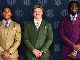 Three men in colorful suits posing in front of an SEC backdrop, smiling at the camera (tan, green, and purple suits)