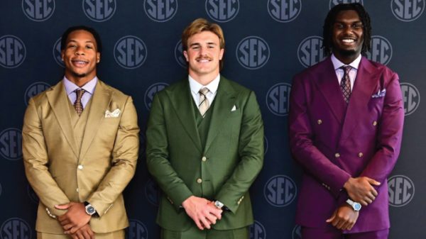 Three men in colorful suits posing in front of an SEC backdrop, smiling at the camera (tan, green, and purple suits)