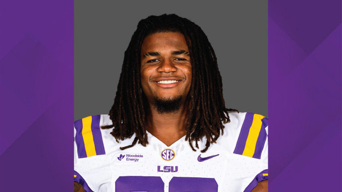 LSU football player smiling in white and purple jersey with LSU logo on gray background.