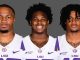 Three LSU football players pose together in white and purple uniforms against a gray backdrop, facing the camera.