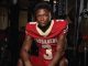 Easton Royal, a Louisiana high school football player in a red jersey with number 3 sits on a weight bench in a gym, looking at the camera.