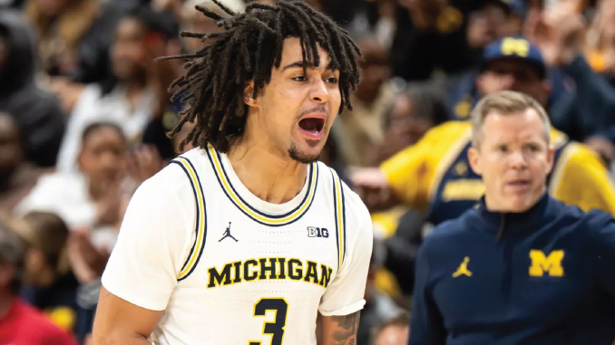 Michigan Wolverines basketball player with dreadlocks, number 3, shouting on the court; coach in blue and maize in the background.