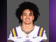 Portrait of a college football player wearing an LSU purple and gold jersey against a gray background.