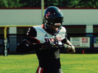 Football player in black and white uniform adjusting gloves on a sunny practice field