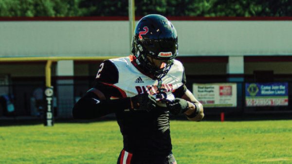 Football player in black and white uniform adjusting gloves on a sunny practice field