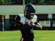 Football player in black and white uniform adjusting gloves on a sunny practice field