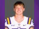 Portrait of a male LSU football player in a white jersey with purple‑and‑gold trim, against a gray backdrop.