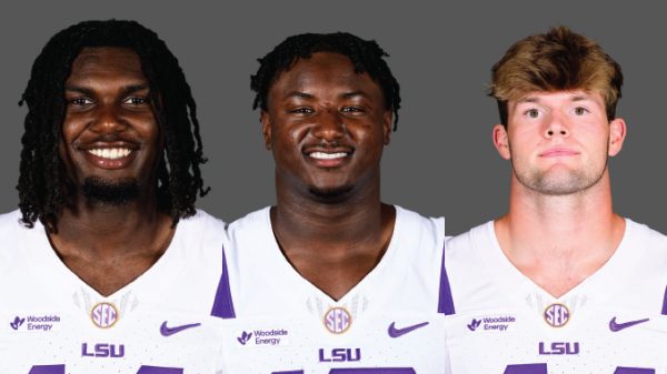 Three LSU football players smiling, wearing white jerseys with purple LSU logos, against a gray backdrop.