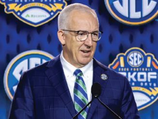 Man in a blue suit and green striped tie speaks at a podium, with SEC logos on a blue backdrop behind him.