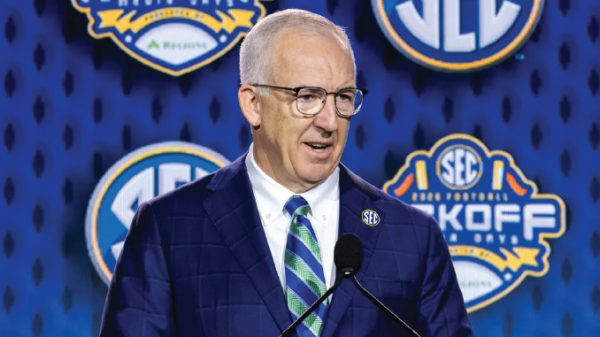 Man in a blue suit and green striped tie speaks at a podium, with SEC logos on a blue backdrop behind him.