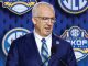Man in a blue suit and green striped tie speaks at a podium, with SEC logos on a blue backdrop behind him.