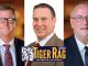 Three men in business suits posing with a Tiger Rag Radio banner for LSU sports in front of them.