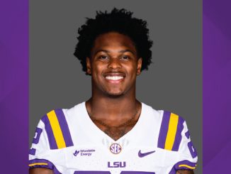 Portrait of an LSU football player in a white jersey with purple and gold stripes, smiling at the camera.