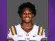 Portrait of an LSU football player in a white jersey with purple and gold stripes, smiling at the camera.