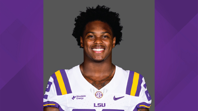 Portrait of an LSU football player in a white jersey with purple and gold stripes, smiling at the camera.