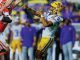 LSU player in purple and gold reaches up to catch a pass as Clemson defenders in orange close in on him.