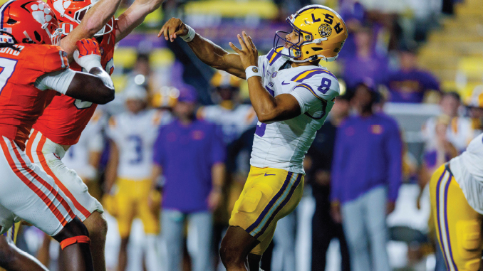 LSU player in purple and gold reaches up to catch a pass as Clemson defenders in orange close in on him.