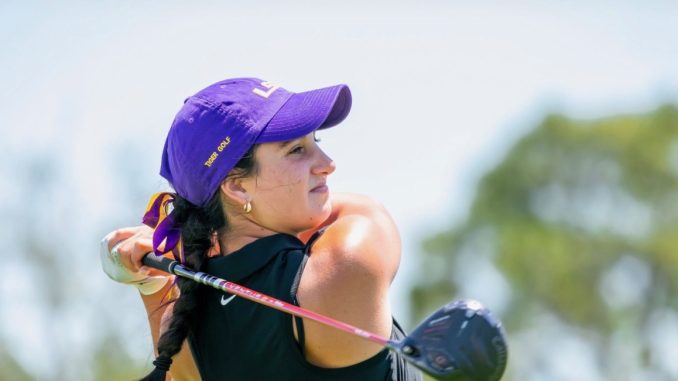 Female golfer in a purple cap swinging a golf club on a sunny course
