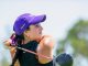 Female golfer in a purple cap swinging a golf club on a sunny course
