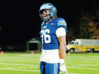 American football player in a blue uniform with the number 76, standing on a well-lit field at night, wearing a helmet and white gloves.