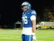 American football player in a blue uniform with the number 76, standing on a well-lit field at night, wearing a helmet and white gloves.