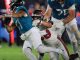 Quarterback in a teal jersey being tackled by a defender in white and red during an NFL game.
