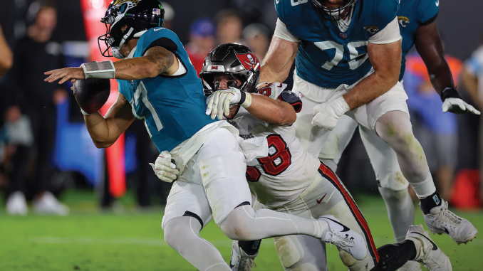 Quarterback in a teal jersey being tackled by a defender in white and red during an NFL game.