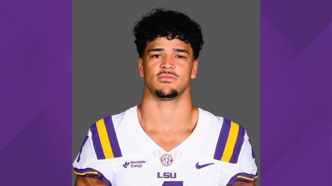 Portrait of a man in an LSU football uniform (white jersey with purple and gold stripes) facing the camera against a gray backdrop.