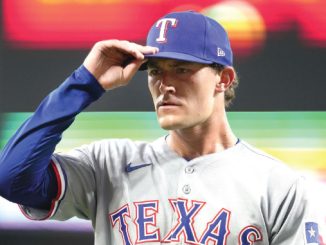 Texas Rangers player in gray uniform tipping his blue cap with a white 'T' while on the field