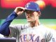 Texas Rangers player in gray uniform tipping his blue cap with a white 'T' while on the field
