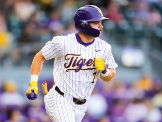 Baseball player in a white pinstripe Tigers uniform runs on the field, wearing a purple helmet and yellow batting gloves.