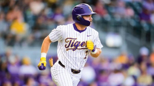Baseball player in a white pinstripe Tigers uniform runs on the field, wearing a purple helmet and yellow batting gloves.