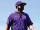 Person in a purple baseball uniform looking off to the right, standing outdoors against a blue sky.