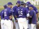 Baseball players in purple uniforms huddle on the field, backs to camera, discussing strategy.