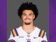 Portrait of a LSU football player in a white jersey with purple and gold stripes, smiling at the camera.