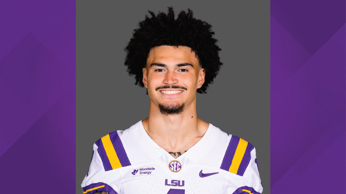 Portrait of a LSU football player in a white jersey with purple and gold stripes, smiling at the camera.