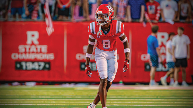 Football player in red and white uniform, number 8, on a football field with fans in the background.